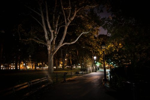 Washington Square Park at night, with a ribbon of the city visible in the distance, the park is dark, and as you will find out haunted!